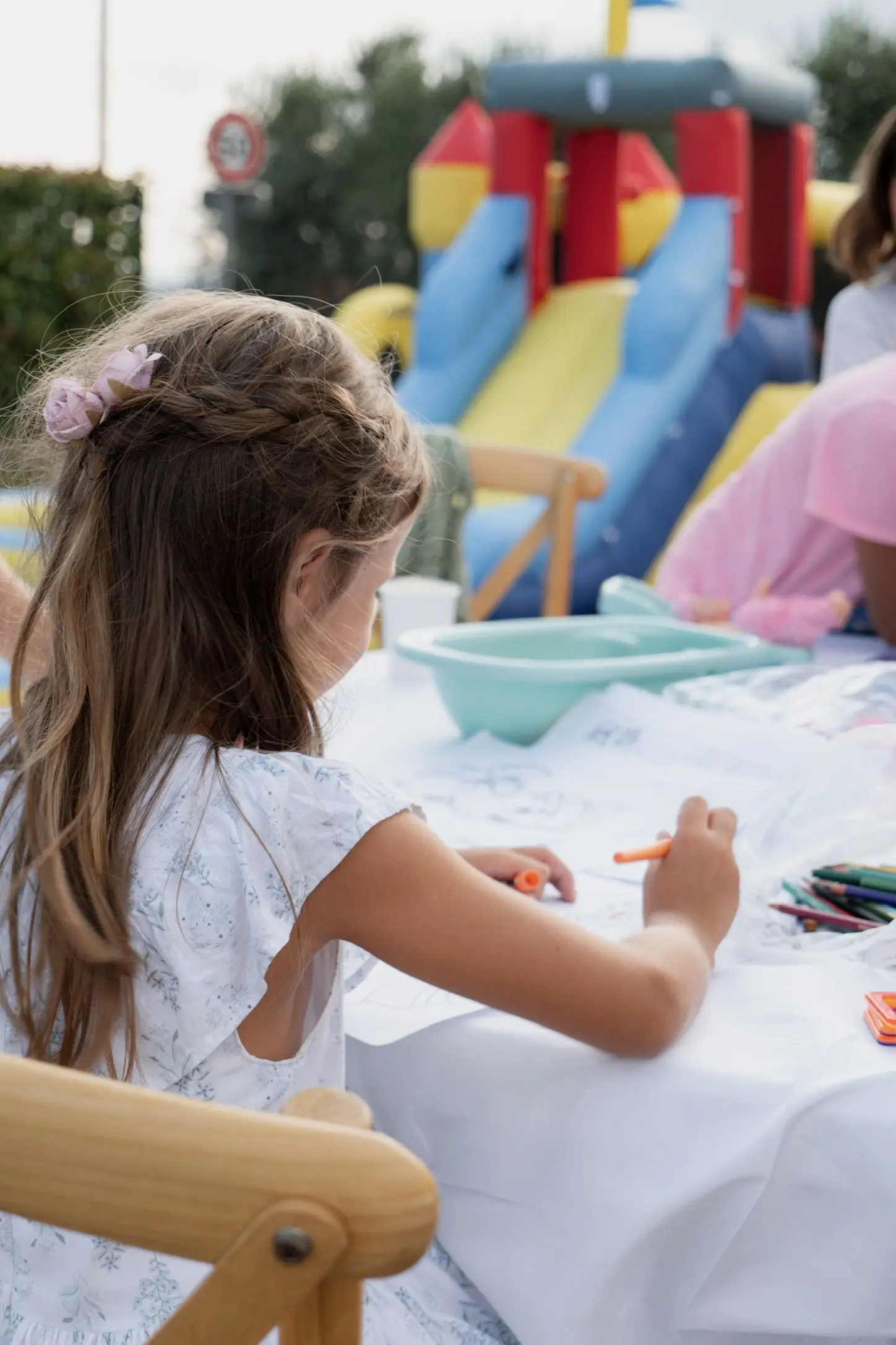 Une petite fille dessine à une table, avec un château gonflable en arrière-plan