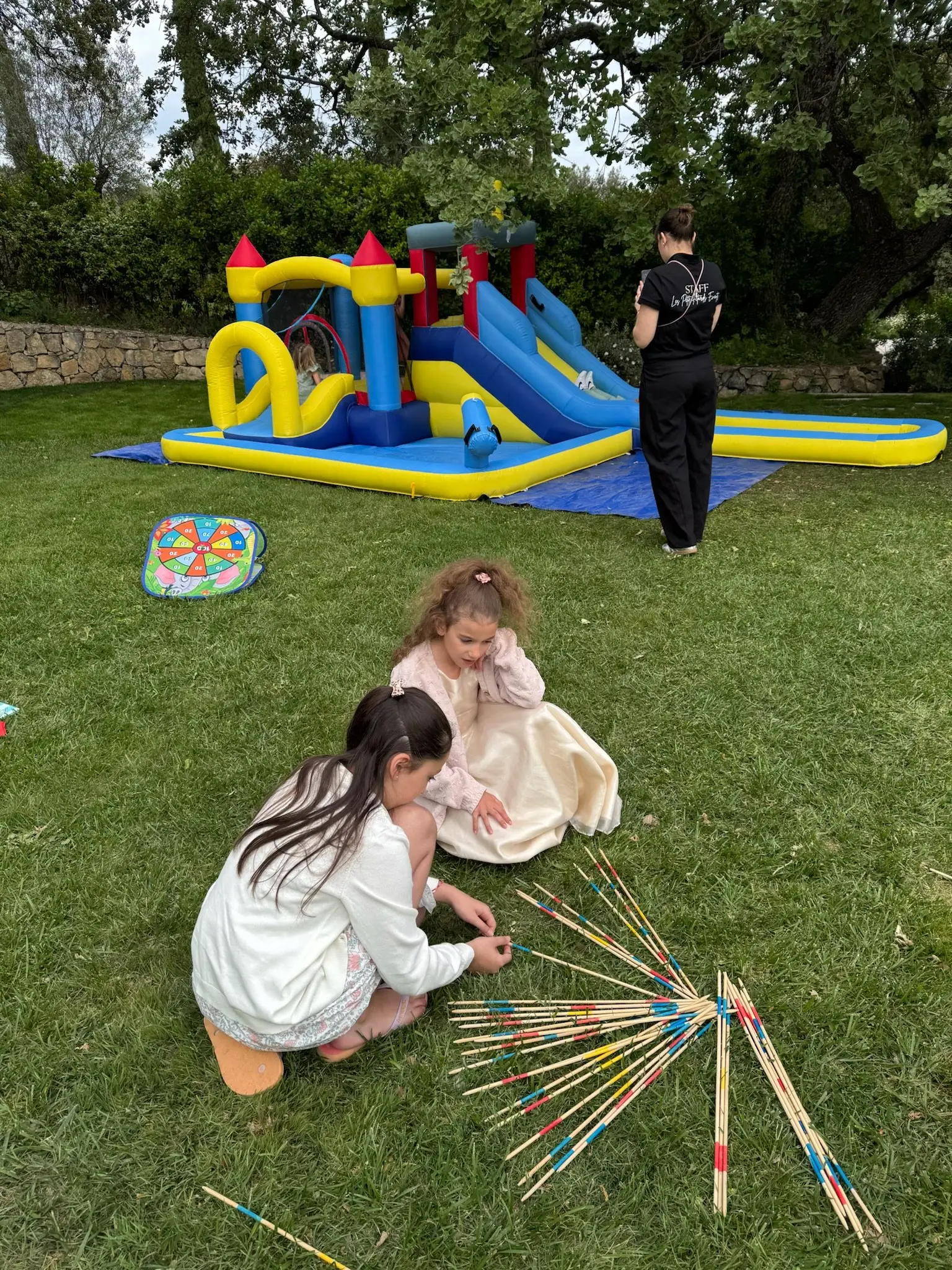 Deux enfants jouent au mikado géant dans l’herbe, près d’une animatrice