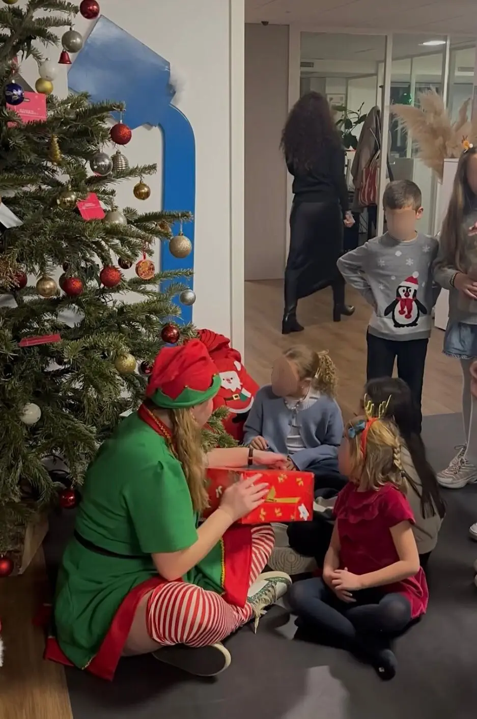 Une animatrice en costume d’elfe accompagne les enfants près du sapin
