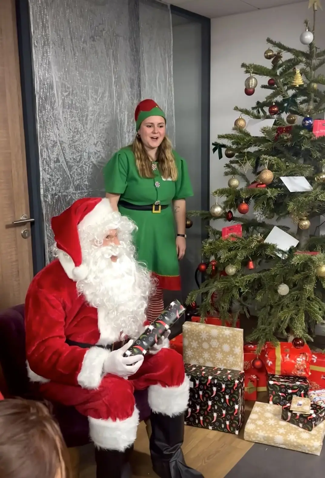 Le Père Noël et une animatrice en costume d’elfe près du sapin et des cadeaux