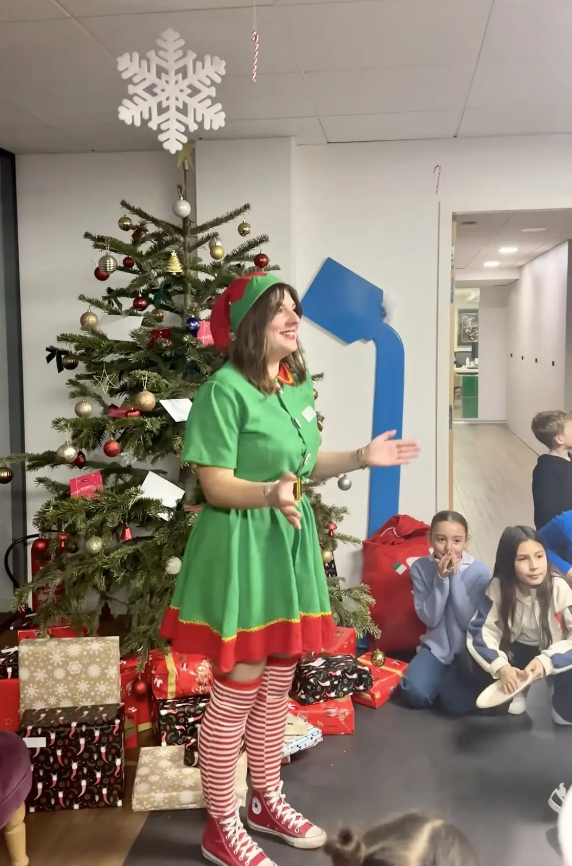 Une animatrice en elfe s’adresse aux enfants réunis devant le sapin