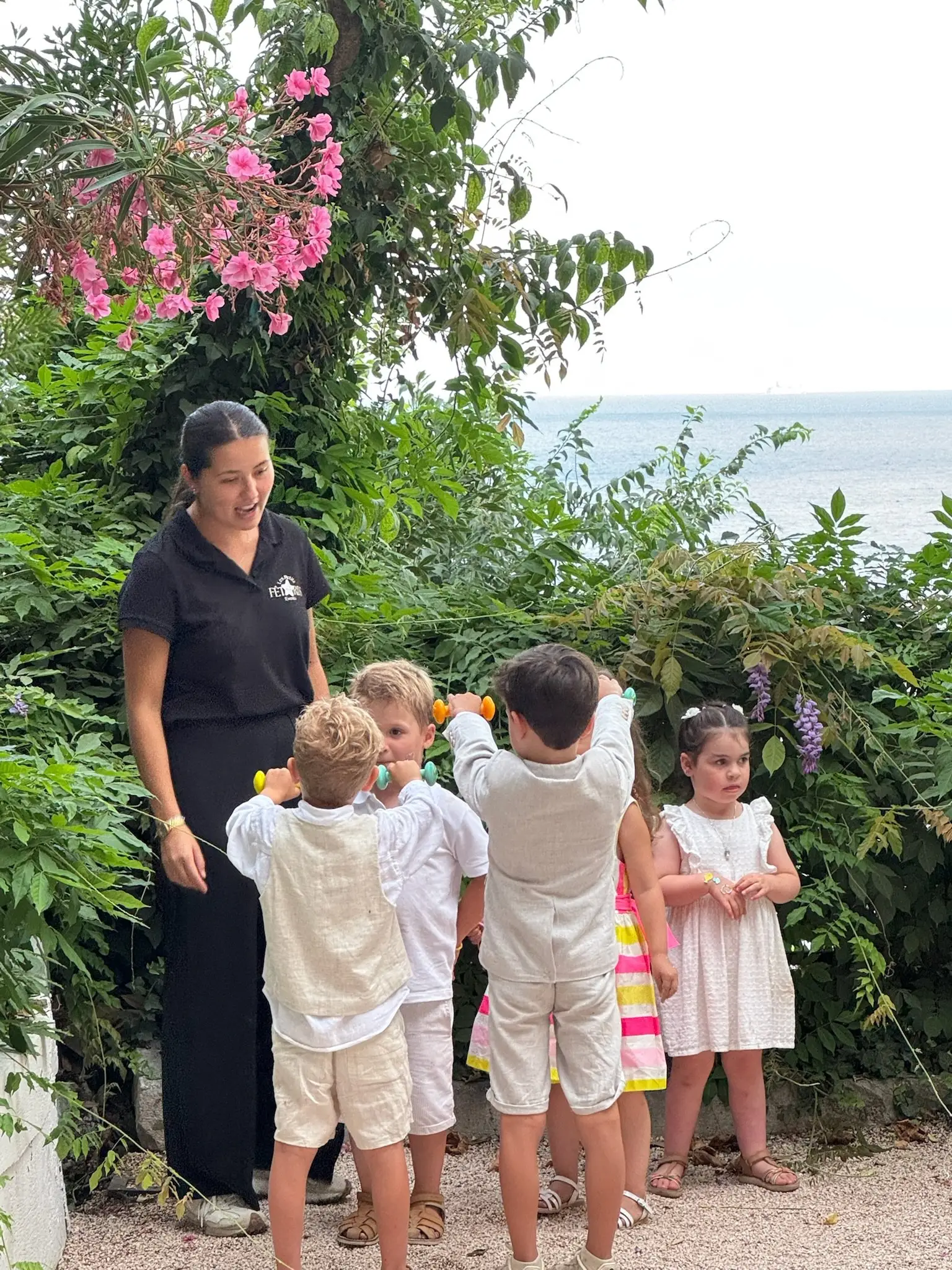 Une animatrice entourée d’enfants devant les lauriers roses, la mer en contrebas