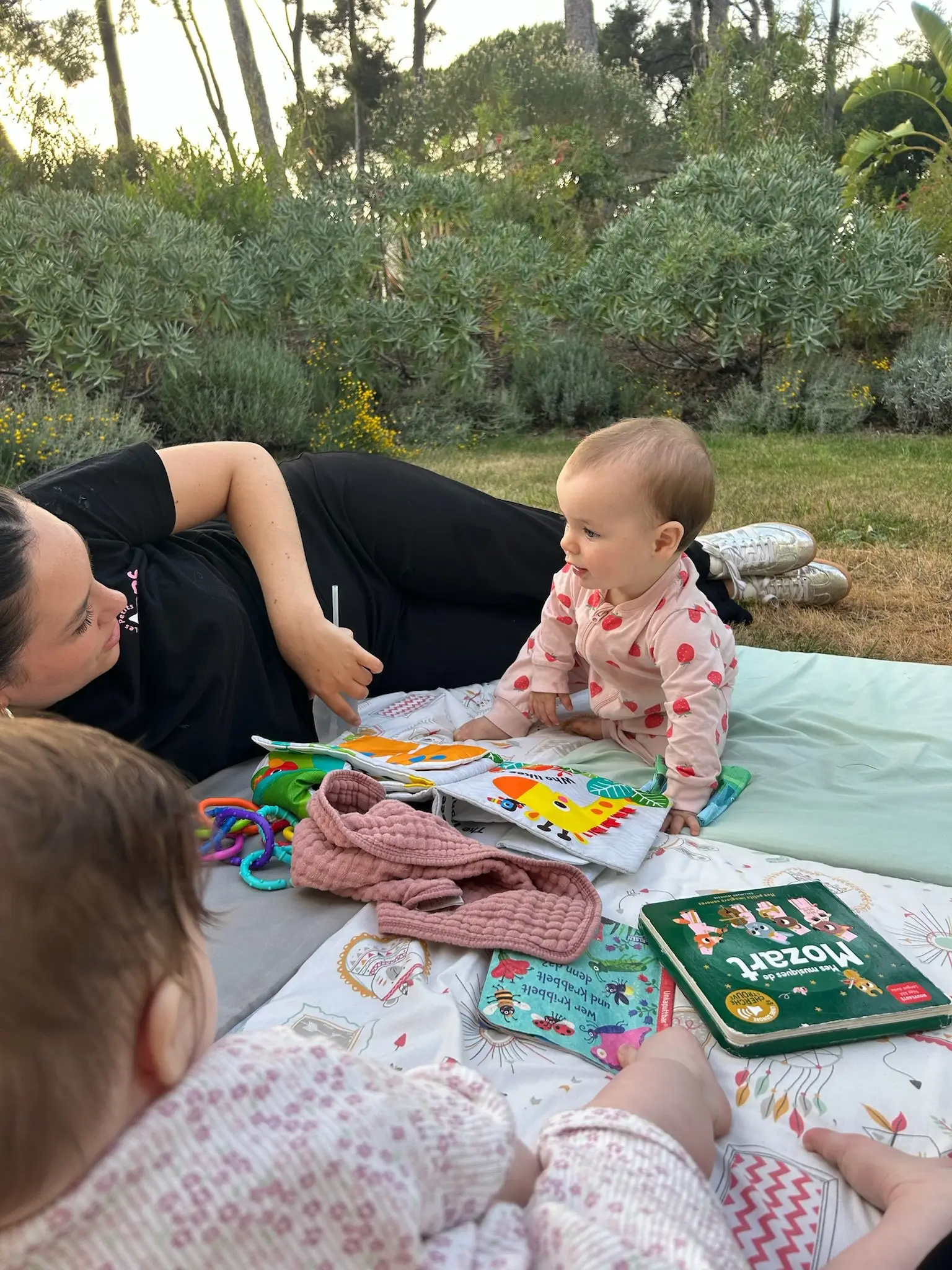 Une animatrice joue avec un bébé sur un tapis d’éveil, dans le jardin