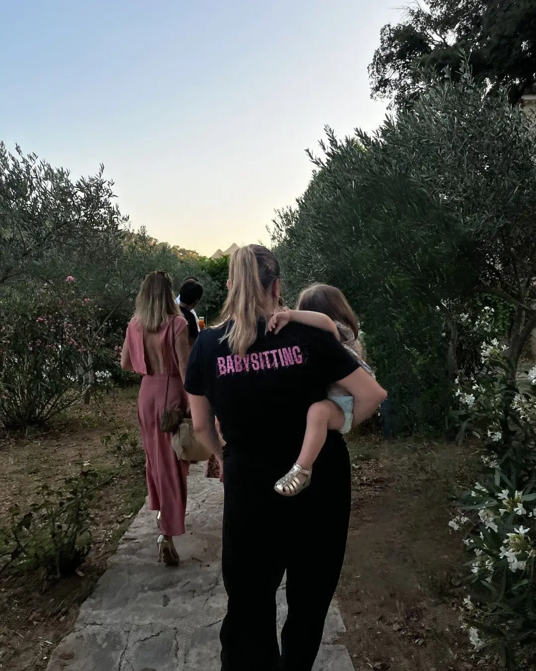 Une animatrice porte un enfant dans un chemin d’oliviers, à la tombée du jour