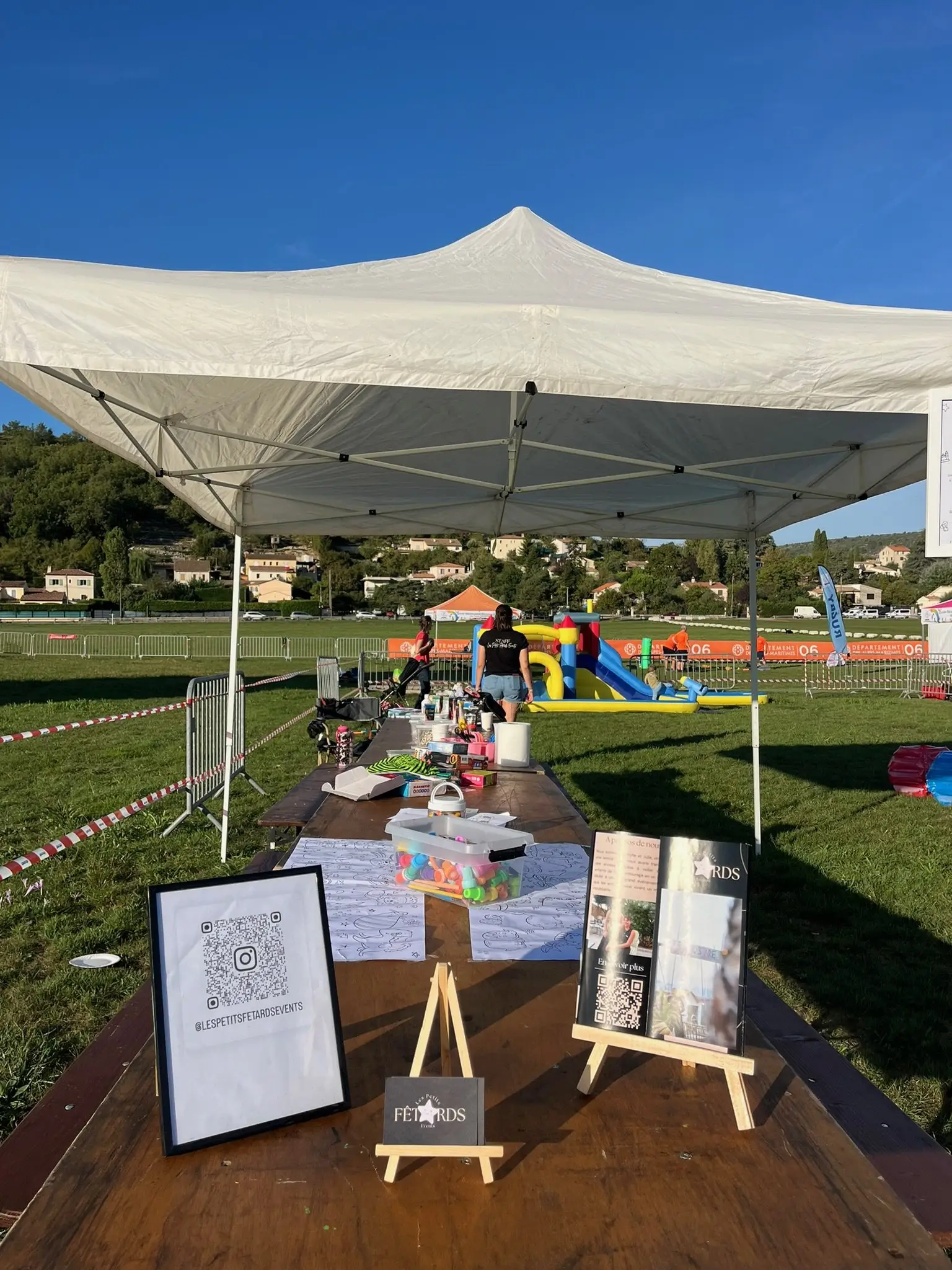 Le stand des Petits Fêtards sous un barnum, avec ses ateliers et une structure gonflable sur la pelouse